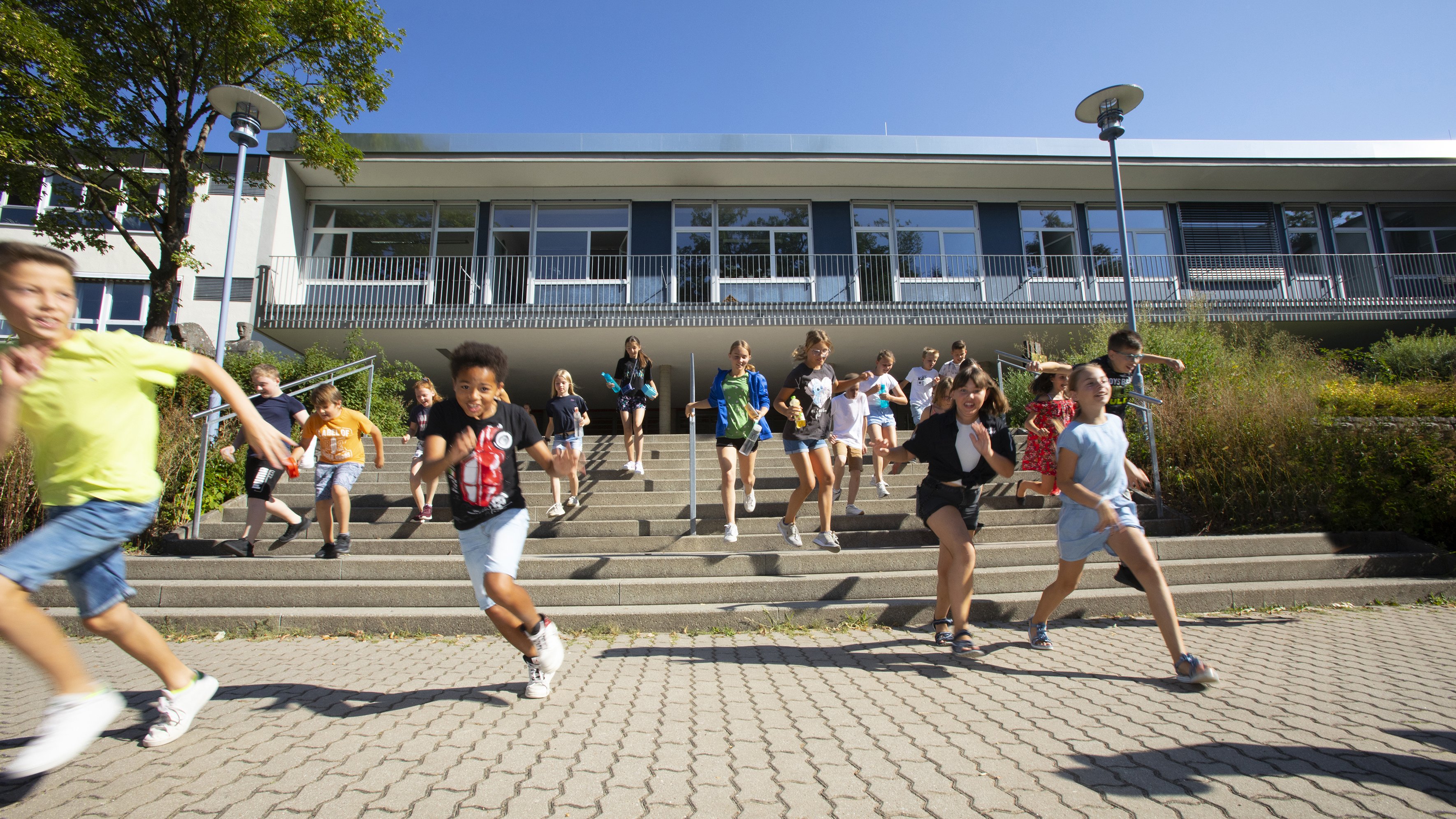 Schülerinnen und Schüler rennen aus dem Schulhaus auf den Schulhof